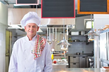 Portrait of smiling mature chef standing against kitchen in restaurant