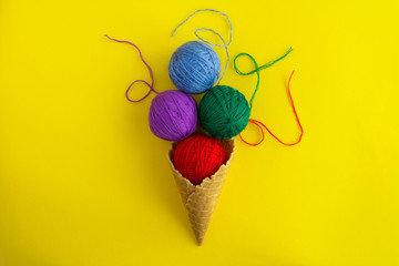Ice cream cone with colorful threads for knitting  in the center of the yellow background. Top view. Copy space.