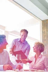 Young waiter showing menu to mature couple at restaurant