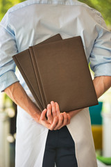 Rear view of young waiter holding menus while standing at restaurant