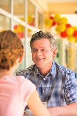 Obraz premium Smiling mature man sitting with young woman at table in restaurant