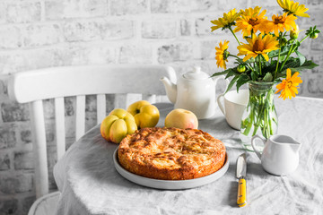 Cozy home tea party table - apple pie, bouquet of yellow flowers, teapot on a light table on a...