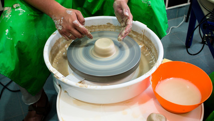 A raw clay pot in the hands of a potter. Workshop in the pottery workshop. Clay pot on a potter`s wheel