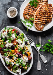 Mediterranean style lunch table - Greek chickpeas salad and pork chops on dark background, top view