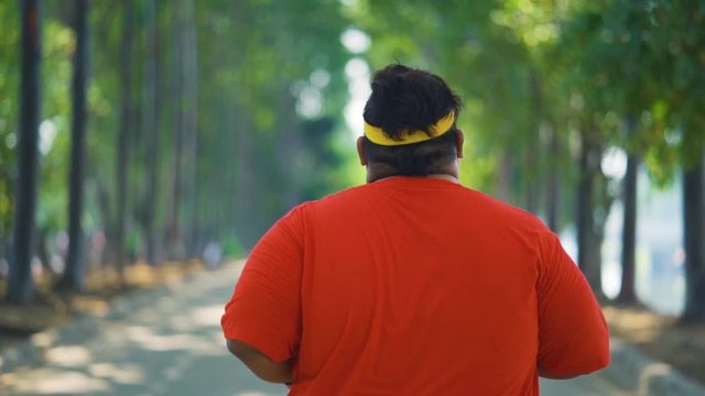 Rear view slow motion of overweight young man jogging for losing weight at the park on the morning