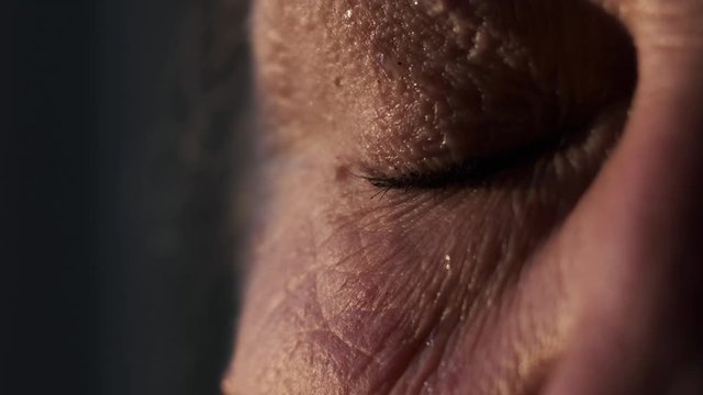 A tear flows down the cheek of an elderly woman, close-up. Grandma is crying, close-up