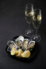 Opened oysters, ice and lemon on stone table. Oyster dinner with champagne in restaurant. Vertical