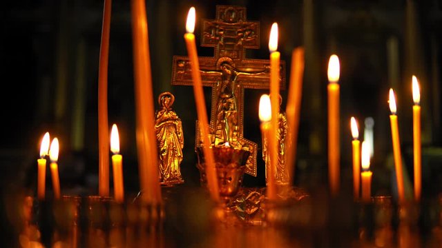Burning candles in the Orthodox Church on background of the Golden crucifixion of Jesus Christ. Pan camera along candlestick table.
