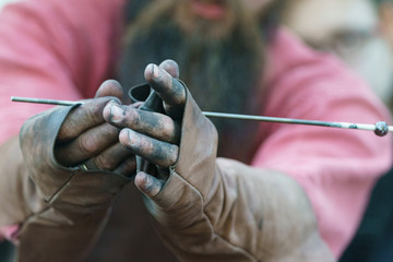 Photography of the process of making beads in the workshop. Man glassblower make handmade products under burner. Ancient Slavic technique depends on bellows fanning.