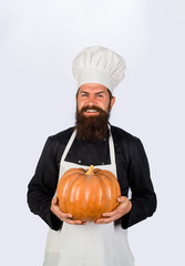 Bearded cook in chef uniform with pumpkin. Chef man in white apron presenting pumpkin for culinary. Thanksgiving seasonal cooking ingredients. Autumn food concept. Healthy organic harvest vegetables.