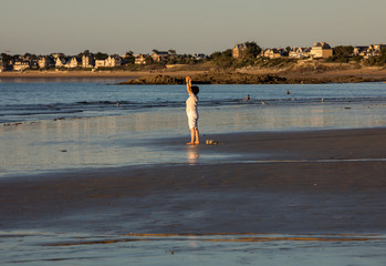 A woman practicing yoga on the beach of Saint Malo in the glow of the setting sun. Brittany, France
