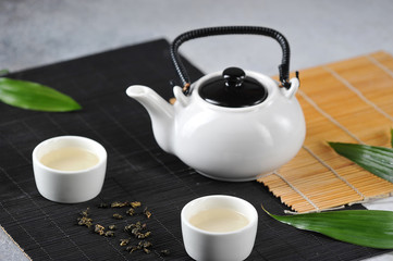 Two white cups of green tea and a teapot on bamboo napkins. Tea ceremony concept. Close-up.