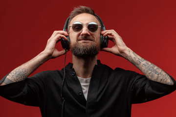 Portrait of a young man in glasses and headphones on a red background.