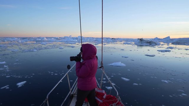 Rear view of tourist photographing Disko Bay while standing in boat at against sky during sunset