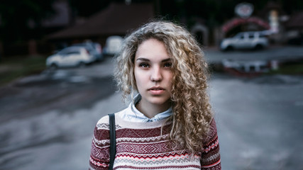 Cute girl: blonde with curly hair, brown eyes, wearing a sweater with patterns on the shirt. Format 16: 9 (film frame), horizontal image. The model is a close-up on a background of the institution.