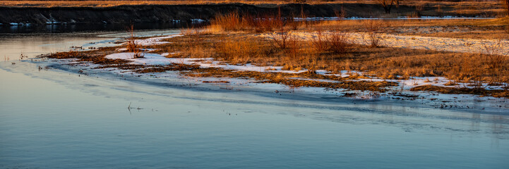 Obraz na płótnie Canvas Water in the River and Shore with Dry Grass at Sunset. Winter Season, February.