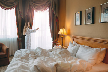 Woman in bathrobe stay near the window in hotel room.