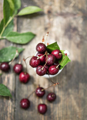 cherry berries in raindrops lie in a mug on a wooden table against a background of greenery