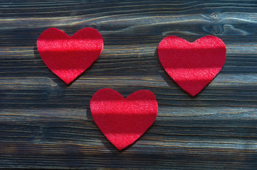 Obraz premium Handmade hearts from red felt with strips of light on dark rustic background. Flat lay