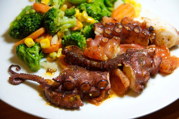 Cooked octopus with vegetables on a plate. Ready to eat sea food meal. Healthy eating concept.