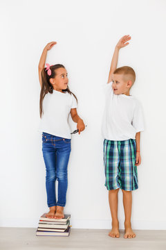 Little boy and girl measuring their height isolated on white background
