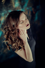 Portrait of young beutiful girl with brown curly hair, weared in black dress,stylish makeup. Studio shot