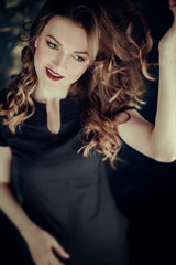 Portrait of young beutiful girl with brown curly hair, weared in black dress,stylish makeup. Studio shot