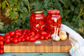 Pickled tomatoes with garlic, onions and spices in glass jars. Fresh tomatoes On a wooden table.