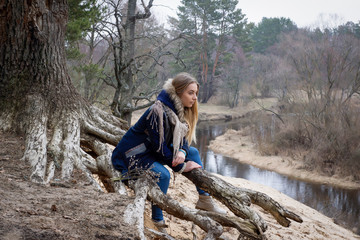 Young beautiful girl in warm clothes walks in the forest in early spring.