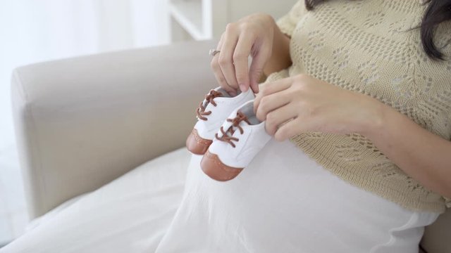 Cropped image of pregnant woman holding baby shoes when sitting on couch
