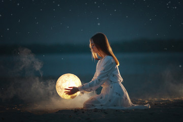 Beautiful attractive girl on a night beach with sand and stars hugs the moon,