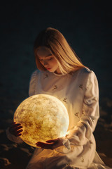 Beautiful attractive girl on a night beach with sand and stars hugs the moon,