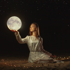 Beautiful attractive girl on a night beach with sand and stars hugs the moon,