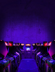 Old Unbranded Vintage Arcade Video Games in dark gaming room with purple light with glowing displays and concrete wall - vertical photo of retro design with free copy space for a poster or magazine - obrazy, fototapety, plakaty