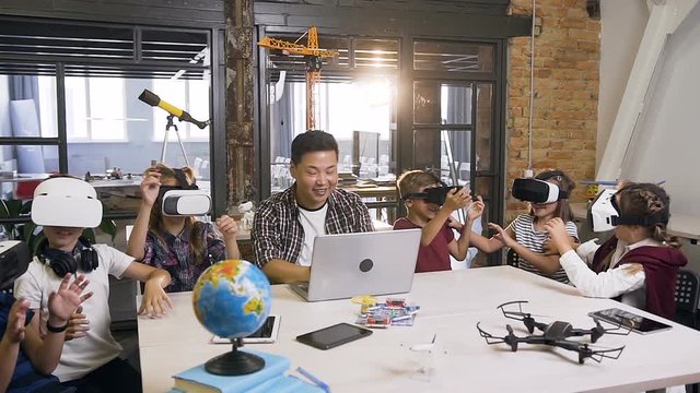 Young Korean teacher with six caucasian young students using augmented reality VR Glasses in a computer science elementary classroom
