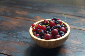 Ripe black and red currants in a wooden bowl on a wooden table. Organic food, harvest season. Top view.