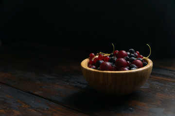 Ripe black and red currants in a wooden bowl on a wooden table. Organic food, harvest season.