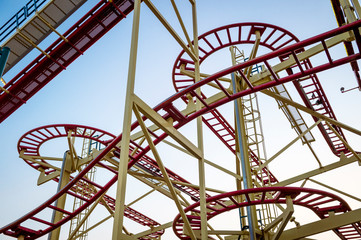Abstract close-up of looping red roller coaster tracks making shapes against clear sky