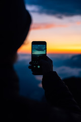 silhouette of person taking a photo of the sunset with a smartphone