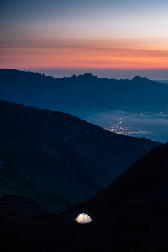 illuminated tent in the mountains with sunrise in the background