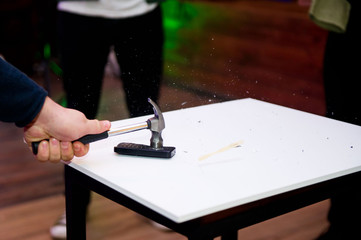 the hammer strikes the old push-button cell phone lying on the table and the fragments fly apart