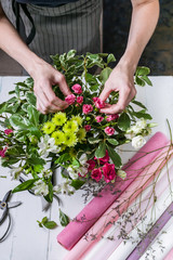 Fototapeta na wymiar Florist at works. Women's hands making a wedding bouquet of roses. Small business concept. Vertical shot