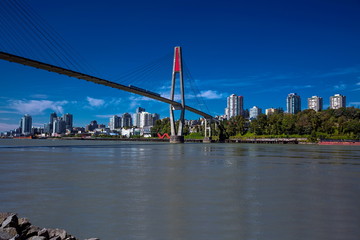 Fototapeta premium Sky-train bridge linking Surrey and New Westminster over the Fraser River, city on the opposite bank, blue sky with white clouds on a background 