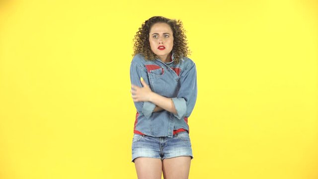 Beautiful girl froze and trying to keep warm on yellow background at studio.