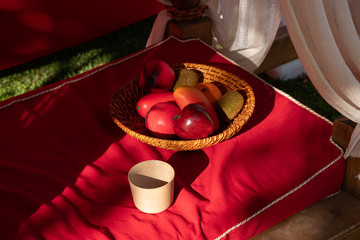 Réplicas de frutas hechas en plástico, en una cesta sobre una mesa con un mantel rojo.