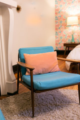 Blue cushion and wood mid century modern chair with pink pillow in bedroom, vintage pink floral wallpaper