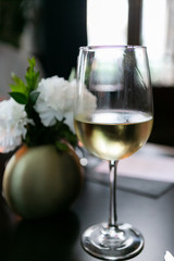 Glass of white wine on restaurant table, flowers in gold vase in background