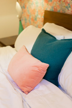 Pink and blue throw pillows on white bed, close up, trendy hotel