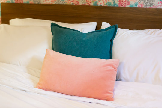Pink and blue throw pillows on white bed, close up, trendy hotel