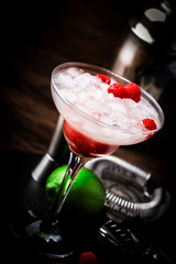 Raspberry daiquiri, alcoholic cocktail with white rum, lime juice, raspberries and crushed ice in tall glass, on wooden bar counter  with steel bar tools